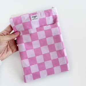May include: Pink and white checkered pouch with a zipper closure. The pouch has a pocket on the front and a small tag that reads "SEPTEMBER SKYE". The pouch is held in a hand.