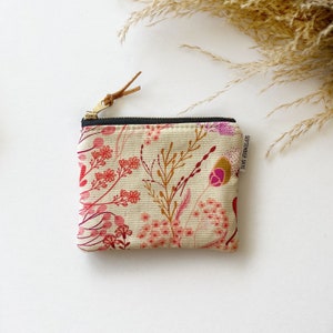 May include: A small, rectangular canvas pouch with a floral pattern in shades of pink, red, and brown on a cream background. The pouch has a black zipper and a leather pull tab. The text "SEPTEMBER SKYE" is printed on the side.