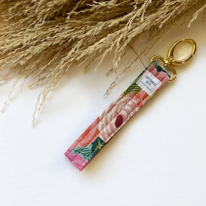 May include: A pink and green floral patterned key chain with a gold metal key ring. The keychain has the text "SEPTEMBER SKYE" and "fancy everything" printed on it.