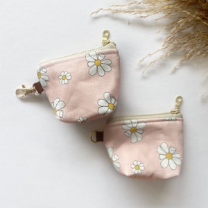 Puede incluir: Dos estuches de cremallera rosa con estampado de margaritas blancas. Los estuches tienen cremalleras doradas y un llavero dorado.