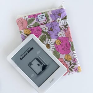 Puede incluir: Un lector de libros electrónicos Kindle blanco con el texto "Editors' picks that are Great on Kindle" y una funda con estampado floral. La funda presenta flores rosas, moradas y amarillas con el texto "SEPTEMBER SKYE".