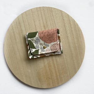 May include: A small floral print fabric pouch with a snap closure. The pouch is on a wooden surface.