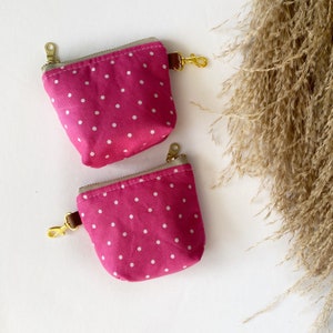 Puede incluir: Dos bolsas de tela rosa con lunares blancos y tiradores de cremallera dorados. Las bolsas tienen una correa de cuero marrón.