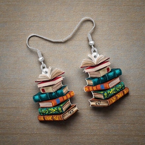 May include: A pair of silver-tone dangle earrings featuring stacks of colorful books. Each earring has a stack of books in shades of red, teal, orange, and green, with open book details at the top. The earrings are designed for book lovers.