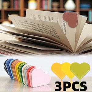 Puede incluir: Un conjunto de marcapáginas en forma de corazón en varios colores, incluyendo rosa, amarillo y azul, con costuras blancas. Un marcapáginas está colocado en un libro abierto. El texto "3PCS" es visible.
