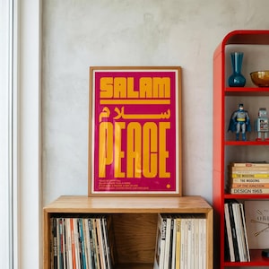 May include: A framed rectangular poster with a magenta background and bold yellow typography. The text reads SALAM in English and Arabic script, followed by the word PEACE. Smaller text below reads: SALAM IS MORE THAN A WORD. IT IS A WAY, A PRAYER, A WAY OF LIFE. SPREAD SALAM. CHOOSE PEACE. LIVE WITH LOVE.