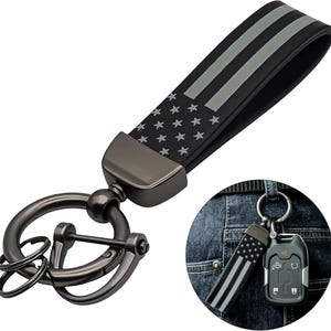 May include: Black key chain with a strap featuring a design of the American flag. The strap has gray stripes and white stars. The key chain has a gunmetal finish and a large ring for keys.