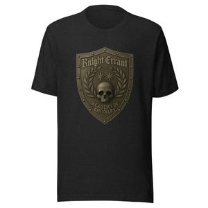 May include: Dark gray t-shirt featuring a shield design with the words "Knight Errant" and "Academy of Chivalry". The shield has a skull, stars, and laurel leaves in a bronze color.