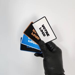 Peut inclure: Une main gantée de noir tient une pile de cartes rectangulaires. Les cartes sont blanches, bleues et marron, chacune portant le mot "LOGO". La carte du dessus porte les mots "VOTRE LOGO".