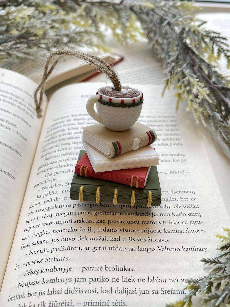 Puede incluir: Un marcap&aacute;ginas caprichoso con una peque&ntilde;a taza de caf&eacute; blanca con una bebida marr&oacute;n y malvaviscos, encima de una pila de tres libros coloridos. El marcap&aacute;ginas est&aacute; hecho de arcilla polim&eacute;rica y tiene una cuerda de yute para colgar.