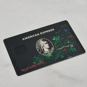 May include: Black American Express credit card with a floral design. The card features the American Express logo, the text "AMERICAN EXPRESS", and the text "YOUR NAME HERE". The card has a CID number and a "MEMBER SINCE" date.