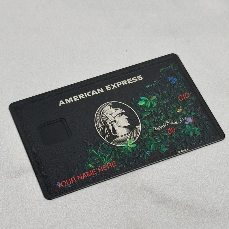 May include: Black American Express credit card with a floral design. The card features the American Express logo, the text "AMERICAN EXPRESS", and the text "YOUR NAME HERE". The card has a CID number and a "MEMBER SINCE" date.