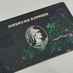 May include: Black American Express credit card with the words "AMERICAN EXPRESS" in white. The card features a profile of a man in a helmet and floral design. The words "MEMBER SINCE" and "AMEX" are also visible.