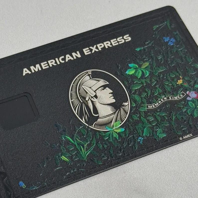 May include: Black American Express credit card with the words "AMERICAN EXPRESS" in white. The card features a profile of a man in a helmet and floral design. The words "MEMBER SINCE" and "AMEX" are also visible.