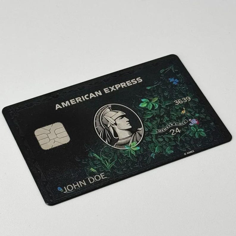 May include: Black American Express credit card with a floral design. The card features the American Express logo, a chip, and the name "JOHN DOE". The card also displays the numbers "3639" and "24", along with the words "MEMBER SINCE".