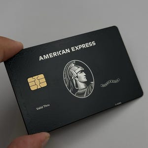Può includere: Una carta di credito American Express nera con il nome dell'azienda in bianco. La carta presenta un chip dorato, un emblema di soldato romano e le parole "Valid Thru" e "Member Since".