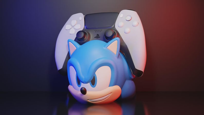 May include: A blue Sonic the Hedgehog figure with a white and black PlayStation 5 controller behind it. The figure has a smiling expression and is set against a dark background with red and blue lighting.