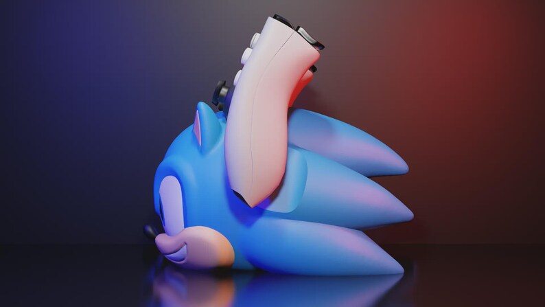 May include: A blue Sonic the Hedgehog figure with a white game controller resting on its head. The figure is lying down on a reflective surface, with a gradient background of red and blue.