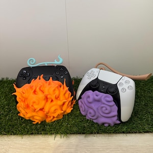 May include: Two custom video game controllers. One is black with orange flame accents and a light blue swirl. The other is white with purple brain-like accents and a tan horn.