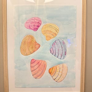 May include: Watercolor art print of six seashells in shades of pink, orange, yellow, and blue, set against a light blue background. The artwork is framed in a light wood frame, creating a coastal theme.