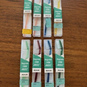 Peut inclure: Plusieurs brosses à dents Squibb 3 Row Angle, emballées individuellement dans des étuis en plastique transparent. Les brosses à dents sont de différentes couleurs, avec une étiquette verte indiquant "MEDIUM".