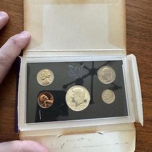 May include: A 1968 United States proof set in its original packaging. The set includes a half dollar, quarter, dime, nickel, and penny, all in brilliant uncirculated condition. The coins are displayed in a clear plastic holder within a cardboard box.