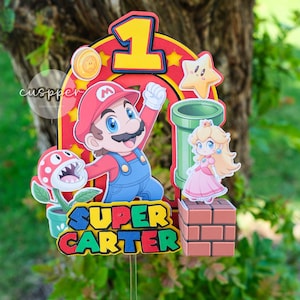Peut inclure: D&eacute;coration de g&acirc;teau sur le th&egrave;me de Super Mario avec Mario, la Princesse Peach, une plante Piranha et un tuyau vert. Le chiffre 1 est mis en &eacute;vidence, avec le nom "SUPER CARTER". Parfait pour une f&ecirc;te d'anniversaire.