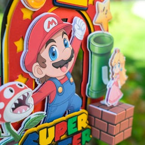 Peut inclure: D&eacute;coration de g&acirc;teau sur le th&egrave;me de Super Mario, avec Mario, la Princesse Peach, une plante Piranha et un tuyau vert. Le dessus de g&acirc;teau comprend le chiffre 1 et le texte "SUPER CARTER" aux couleurs vives, parfait pour un anniversaire.