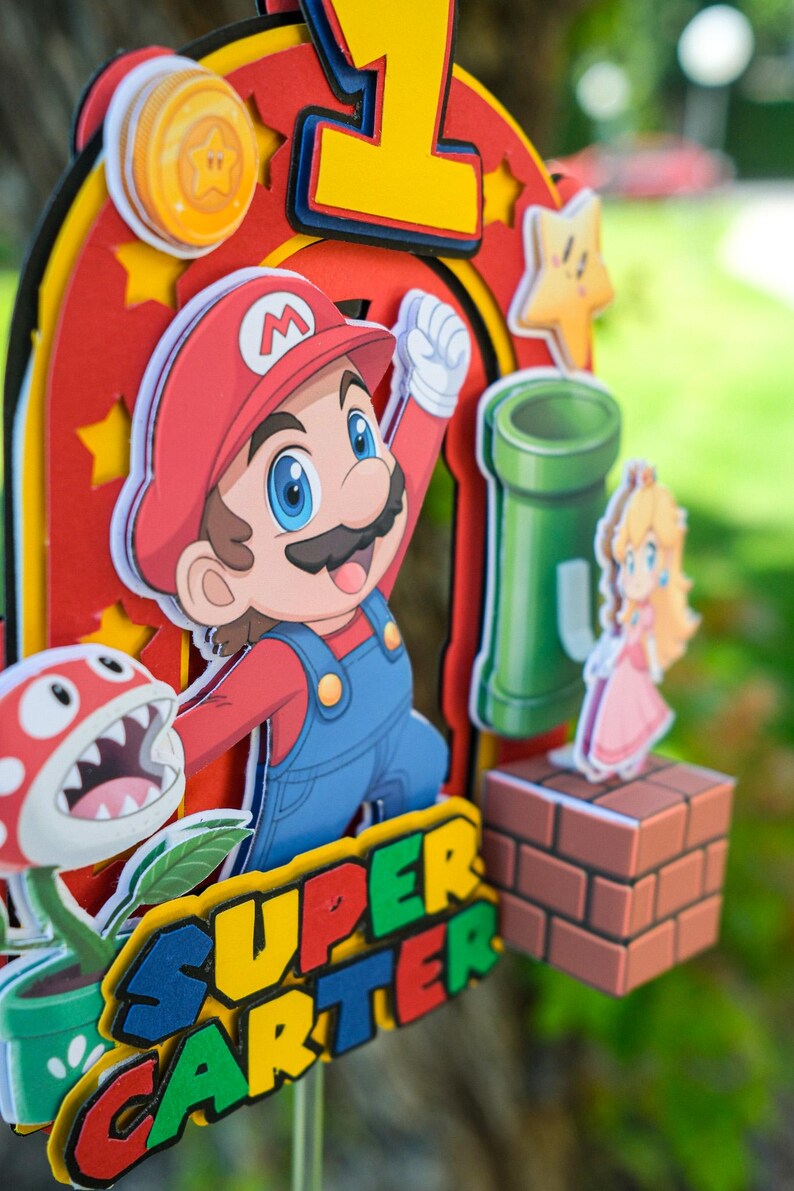 Peut inclure: D&eacute;coration de g&acirc;teau sur le th&egrave;me de Super Mario, avec Mario, la Princesse Peach, une plante Piranha et un tuyau vert. Le dessus de g&acirc;teau comprend le chiffre 1 et le texte "SUPER CARTER" aux couleurs vives, parfait pour un anniversaire.