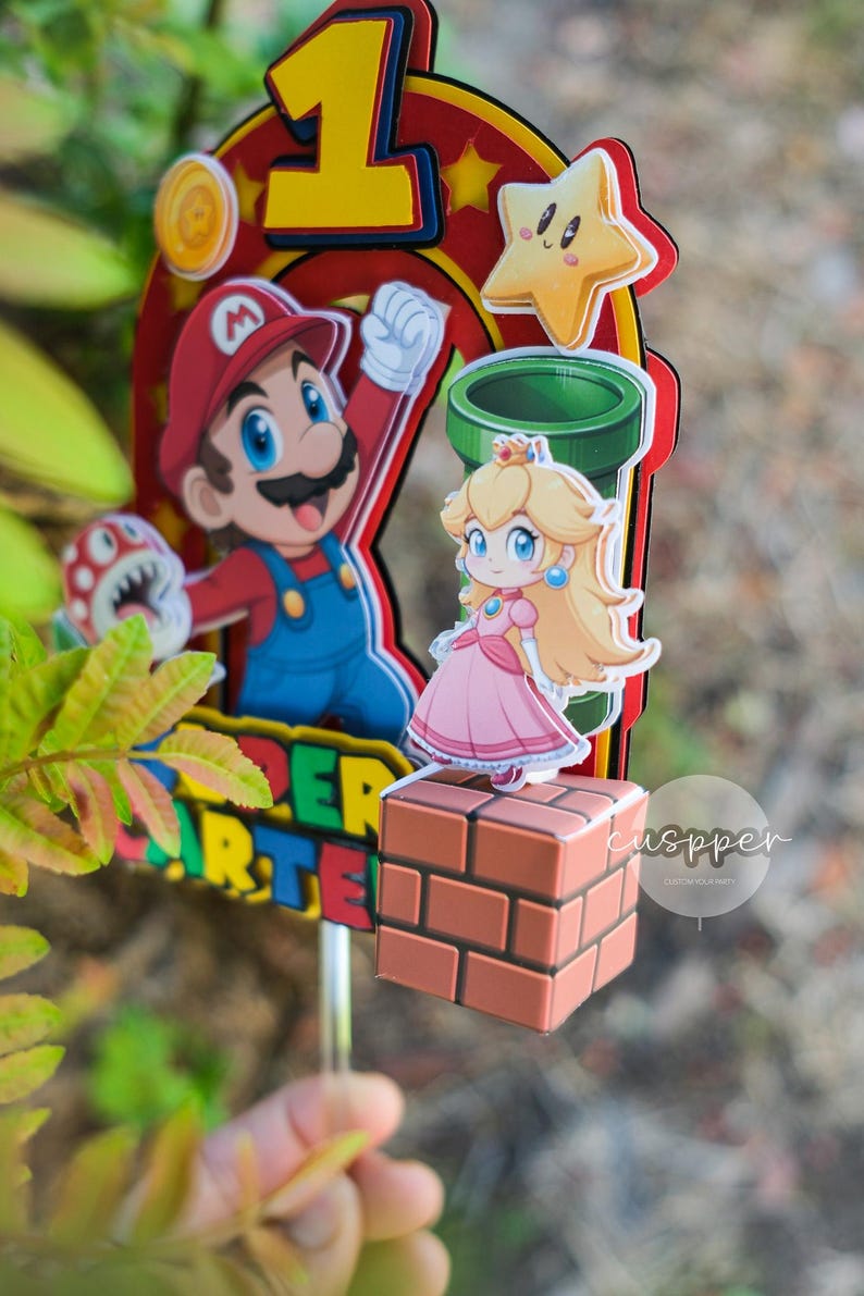 Peut inclure: D&eacute;coration de g&acirc;teau color&eacute;e avec Mario, la Princesse Peach et d'autres personnages de Super Mario Bros. La d&eacute;coration comprend un grand chiffre 1, une &eacute;toile, une pi&egrave;ce et les mots "Super Mario" dans un design vibrant. Les personnages sont sur fond rouge et jaune.