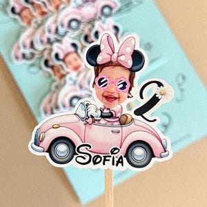 May include: A custom cake topper featuring a cartoon-style illustration of a child with a photo-realistic face, wearing Minnie Mouse ears and flower-shaped sunglasses, driving a pink convertible car with the name Sofia and the number 2.