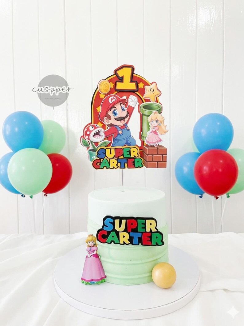 Peut inclure: Un g&acirc;teau d'anniversaire sur le th&egrave;me de Super Mario, avec un d&eacute;grad&eacute; vert et blanc. Le g&acirc;teau est d&eacute;cor&eacute; d'un topper Mario, d'une figurine de la princesse Peach et du texte "SUPER CARTER". Des ballons rouges, bleus et verts compl&egrave;tent l'ensemble festif.
