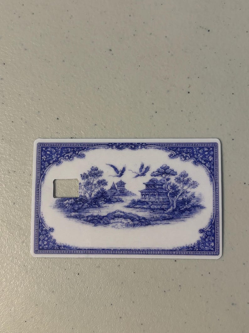 May include: A rectangular card with a blue and white landscape design. The design features a bridge, buildings, trees, and flying birds. The card has a keyhole-shaped cutout on the left side and a decorative border.