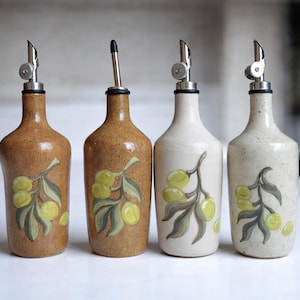 May include: Four ceramic olive oil bottles with stainless steel spouts. The bottles are in shades of brown and white, each decorated with a painted olive branch design. A decorative kitchen item.