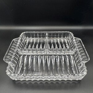 May include: A clear glass divided serving dish with a rectangular shape and three distinct compartments. The dish features a textured pattern of vertical raised ridges on the base and a scalloped edge along the outer rim and handles.