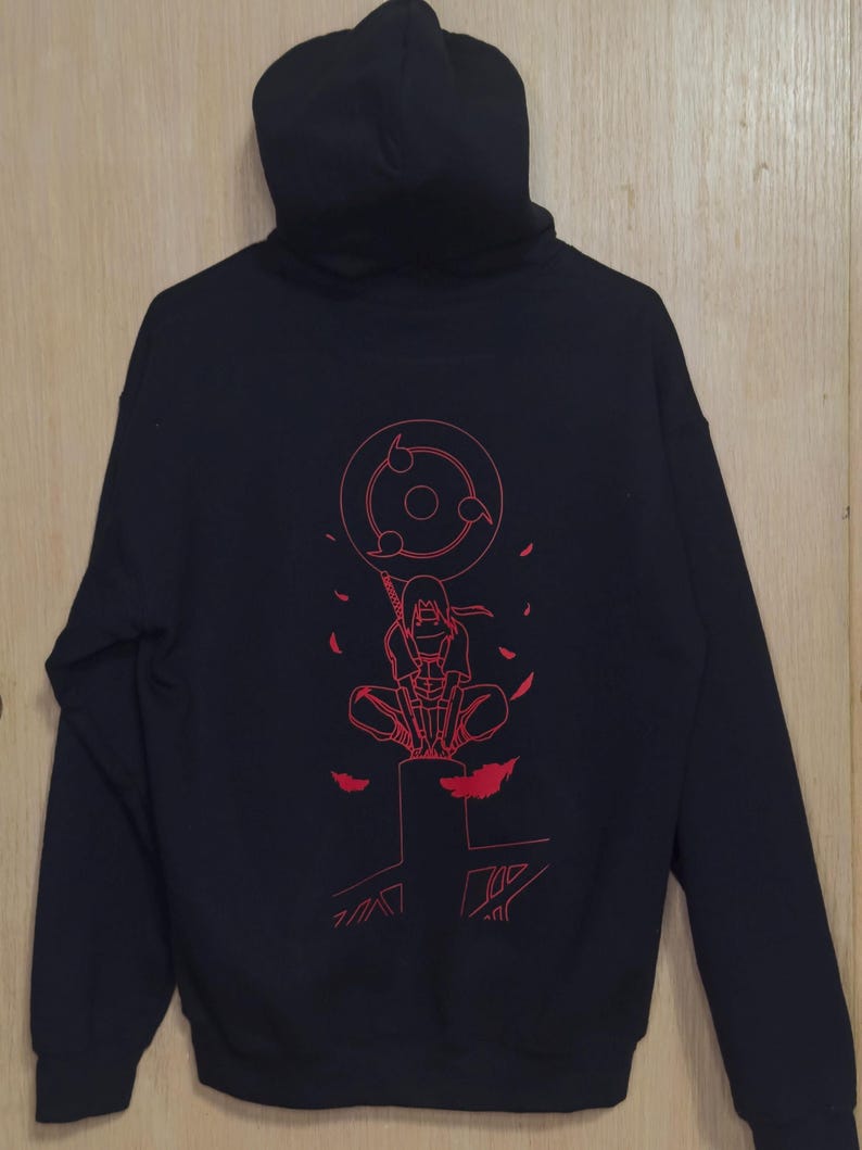 May include: Black hooded sweatshirt with a red graphic on the back. The graphic features a character with a circular design and other elements. The sweatshirt has a hood and long sleeves.
