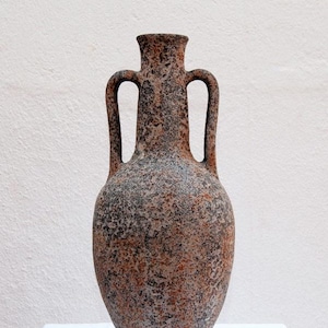 Könnte beinhalten: Eine hohe Vase im Amphorenstil mit zwei symmetrischen Henkeln, die vom Hals bis zur Schulter reichen. Die Oberfläche weist ein gesprenkeltes, strukturiertes Finish in gebranntem Orange, Anthrazit und Erdbraun auf, was ihr ein verwittertes Aussehen verleiht.