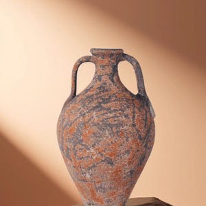Può includere: Un vaso ad anfora rustico con due manici e superficie strutturata. Il vaso presenta un motivo screziato in tonalità grigie e rosso-arancio. È esposto su una base simile a pietra, su uno sfondo caldo e neutro.