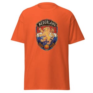 May include: An orange short-sleeve t-shirt featuring a central graphic of a stained-glass style crest. The crest displays a golden lion, a soccer ball, and the text "NEDERLAND" at the top with "VOETBAL SINDS 1889" in smaller print below it.