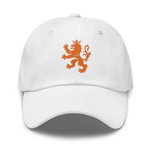 May include: A white baseball cap featuring an embroidered orange lion rampant design on the front center. The cap has a structured crown, a curved brim, and a button at the top. The lion is depicted in a profile view with a crown on its head.