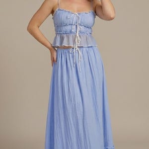 May include: A light blue two-piece set featuring a ruffled crop top with spaghetti straps and a matching floor-length skirt. The top has a tie detail at the bust, and the skirt has a ruffled hemline. The fabric appears to be lightweight and textured.