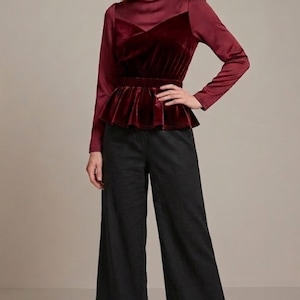 May include: A burgundy velvet peplum top with long sleeves and a high neckline paired with black wide-leg trousers. The top has a satin yoke and a fitted waist. The outfit is completed with black pointed-toe heels.