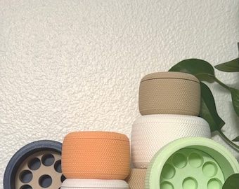 May include: A collection of cylindrical containers with a textured herringbone pattern on the exterior. The set includes various colors such as beige, white, orange, light green, and dark blue, with some lids featuring internal circular compartments.