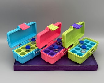 May include: Four colorful, small, plastic cases with hinged lids, each holding small glass vials. The cases are blue, pink, and green, with matching colored latches. The vials have blue or green caps.