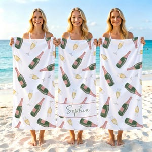 May include: A white beach towel featuring a repeating pattern of champagne bottles and flutes. The center towel includes a horizontal band with the name Sophia printed in a cursive script. The design uses shades of green, pink, and gold.