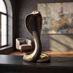 Könnte beinhalten: Eine Kobra-Figur mit aufgerichtetem Nackenschild und geringeltem Schwanz. Die Skulptur ist in einer zweifarbigen Metallic-Optik gehalten, die dunkel anthrazitfarbene Schuppen mit goldenen Akzenten an den Rändern und dem strukturierten Muster kombiniert.