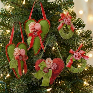 May include: Christmas tree decorations in heart and wreath shapes. The heart ornaments are green and red with pink floral accents and red ribbon. The wreath ornaments are green with red ribbon and pink floral accents.
