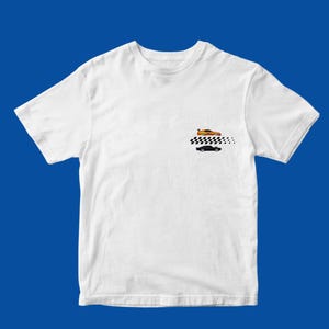 Może przedstawiać: Biały t-shirt z krótkim rękawem z małą grafiką na lewej piersi. Grafika przedstawia pomarańczowy samochód sportowy nad czarno-białym wzorem szachownicy, z czarnym samochodem typu muscle car umieszczonym pod wzorem w szachownicę.