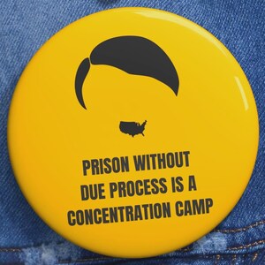 Pode incluir: Um botão amarelo com uma silhueta preta de penteado e um mapa dos Estados Unidos. O texto no botão diz: "PRISÃO SEM DEVIDO PROCESSO É UM CAMPO DE CONCENTRAÇÃO."