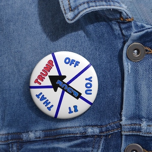 May include: A circular white pinback button featuring a black arrow pointing toward the word TRUMP in red letters. The button is divided into sections by blue lines with the blue text OFF, YOU, IT, and THAT arranged around the center.